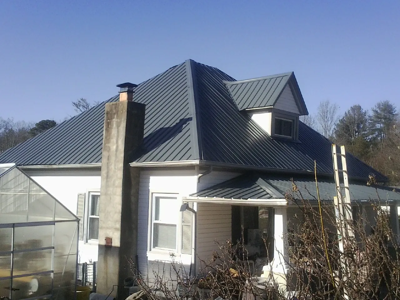 Dark blue standing seam metal roof on a white farmhouse with dormer — Slate & Tile Roof Repair by Roofing Brothers in Weedsport