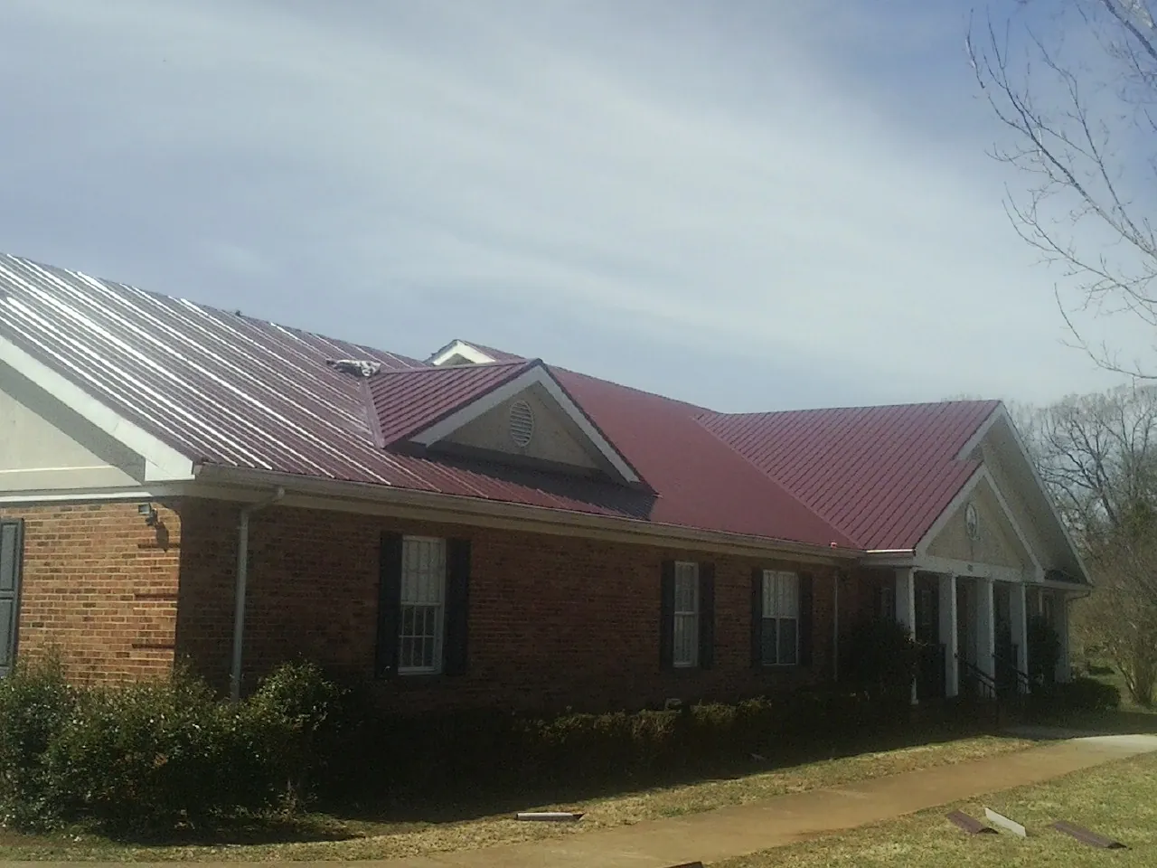 Red metal roof with gabled entries on a long brick building, from a Hail Damage Roof Repair job in Weedsport
