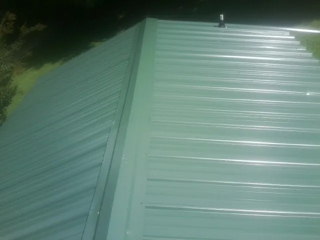 New green metal panels meeting at the ridge of a roof — Flat Roof Repair work by our crew in Weedsport
