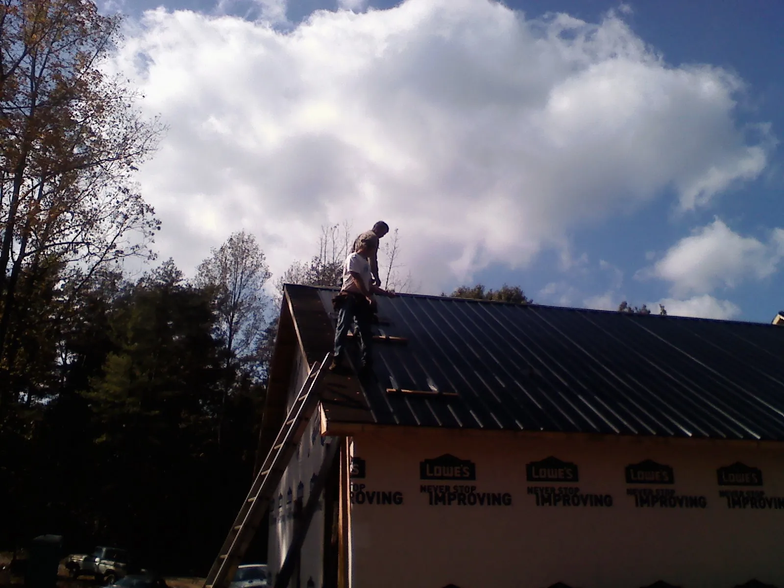 Roofer fastening dark metal panels high against a cloudy sky, from a Roof Inspection job in Weedsport