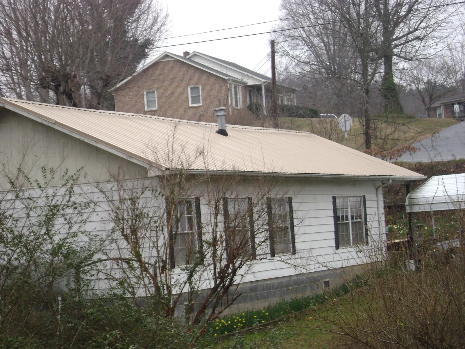 Tan metal roof on a white sided house set into a hillside — Commercial Roofing by Roofing Brothers in Weedsport