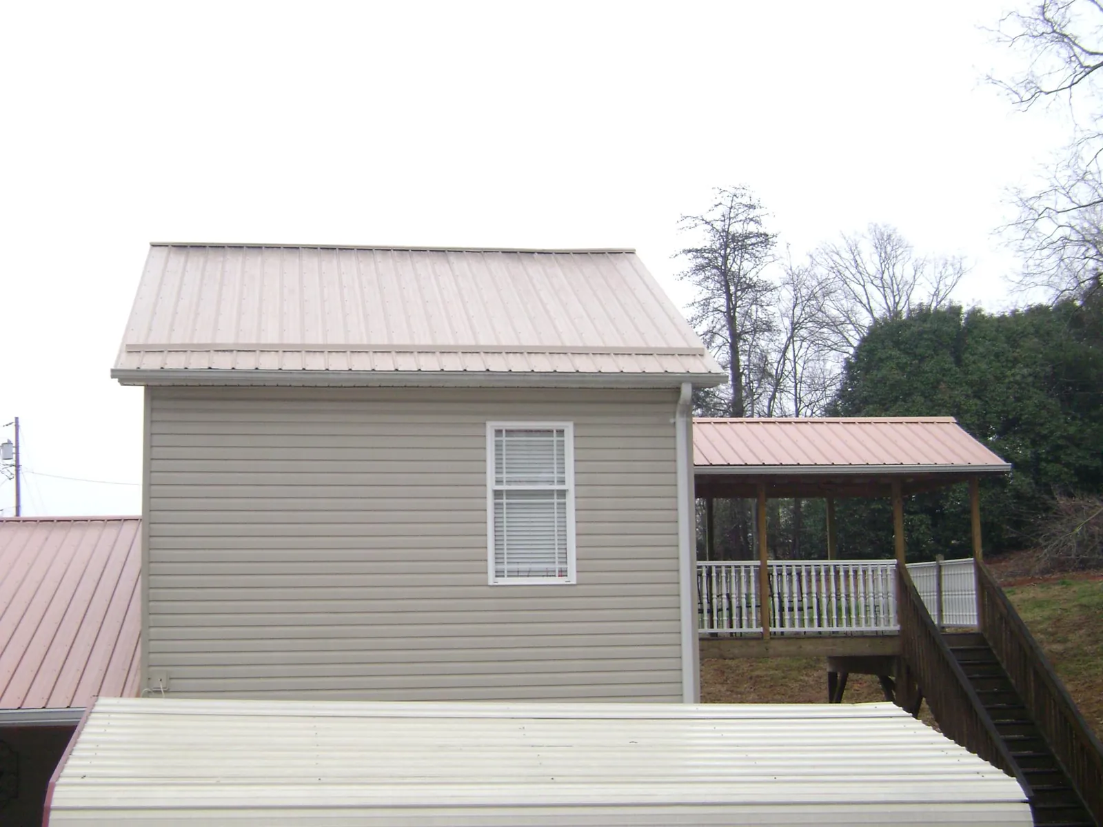 Tan metal roofs on a two story addition and attached porch, from a Roof Replacement job in Weedsport
